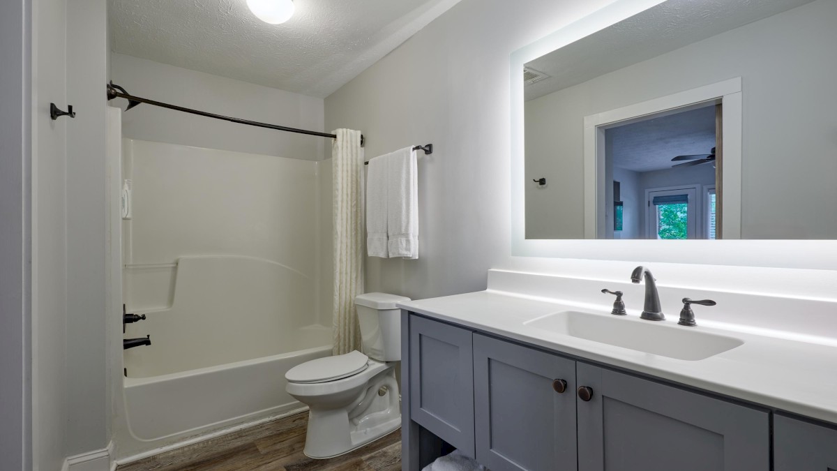 A modern bathroom with a bathtub, toilet, large mirror, and sink on a wooden floor with neatly arranged towels.