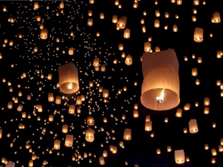 A night sky is filled with numerous glowing floating lanterns, creating a mesmerizing and enchanting scene against the dark background.
