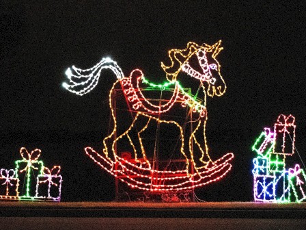 A unicorn-shaped rocking horse and wrapped gifts are depicted in colorful holiday lights.
