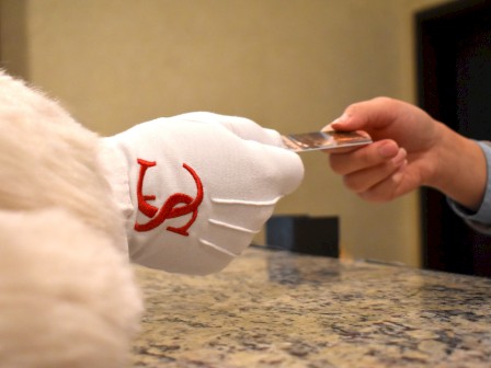 A person in a white glove with red embroidery exchanges a card with another person across a granite counter, suggesting a transaction.