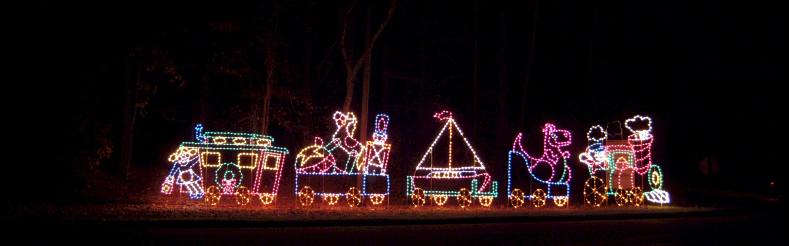 A colorful light display features a whimsical train with animal and boat shapes against a dark background.