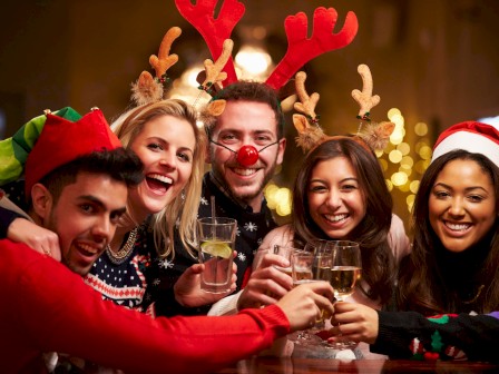 A group of friends wearing festive outfits and reindeer antlers are joyfully toasting with drinks during a holiday celebration.