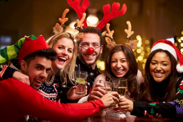 A group of friends wearing festive outfits and reindeer antlers are joyfully toasting with drinks during a holiday celebration.