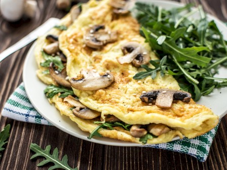 A plate with a mushroom omelette and a side of fresh arugula on a wooden table.