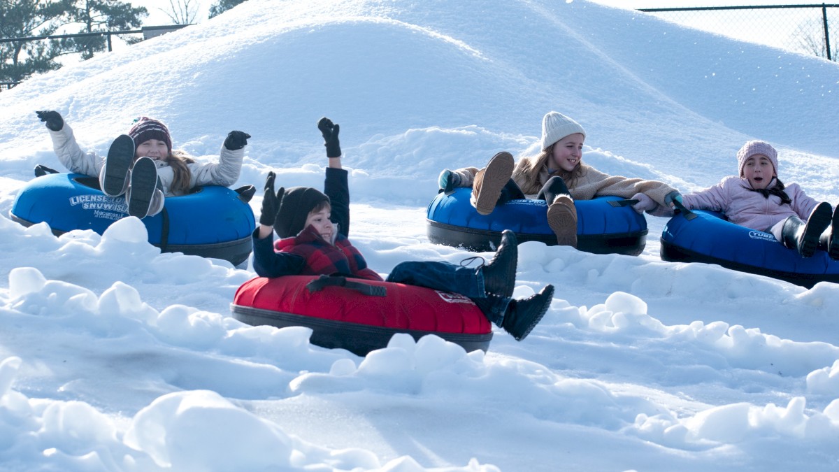 People are enjoying snow tubing, sliding down a snowy hill on colorful inflatable tubes, having fun in a winter setting.