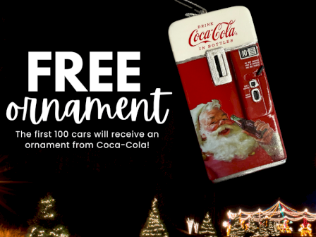 The image advertises free Coca-Cola ornaments for the first 100 cars, featuring a vintage vending machine design with Santa Claus, at night with holiday lights.