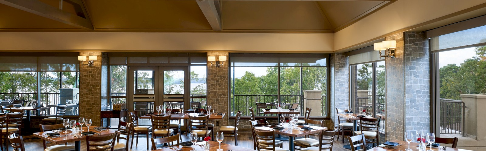 Restaurant dining area with wooden floors, multiple tables and chairs, large windows, and warm lighting. A bright, airy space for meals.