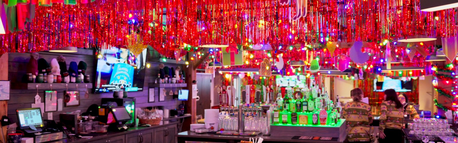 Colorful bar or nightclub with rainbow streamers, bright lights, neon decorations, and a lively drink service counter.
