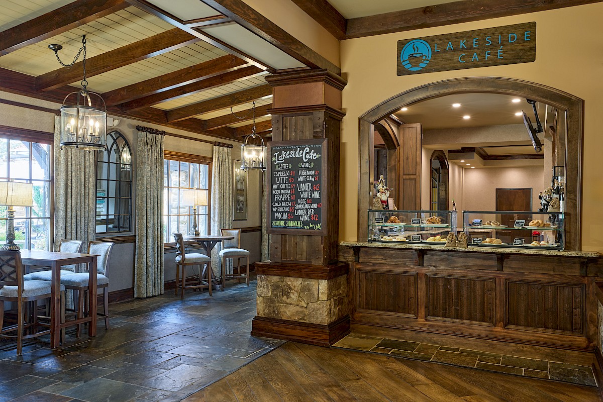 A cozy cafe interior with wooden beams, chalkboard menu, windows with curtains, and a pastry counter labeled 