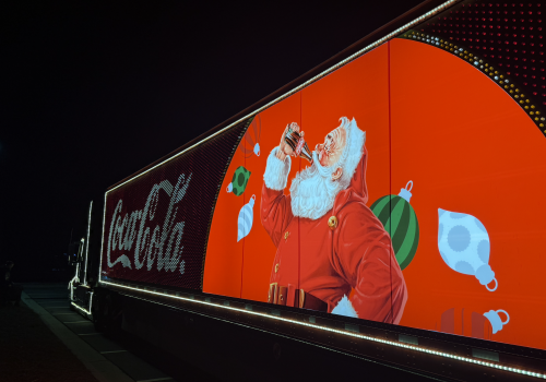 A brightly lit billboard features Santa Claus drinking a soda, surrounded by Christmas ornaments, with a 