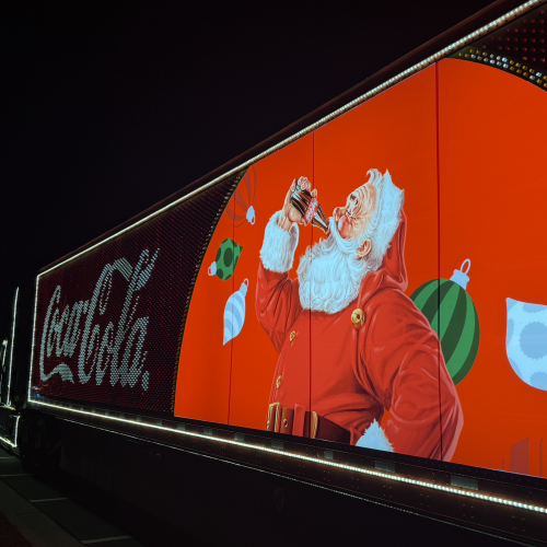 A brightly lit billboard features Santa Claus drinking a soda, surrounded by Christmas ornaments, with a 
