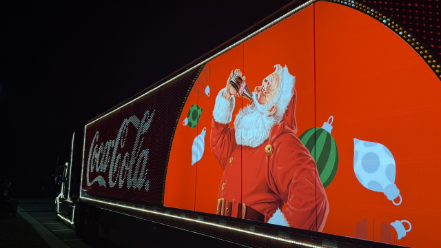 A brightly lit billboard features Santa Claus drinking a soda, surrounded by Christmas ornaments, with a 