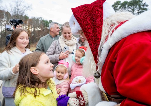 Santa Claus greets children outdoors, sharing a joyful moment during a festive event on a cloudy day.
