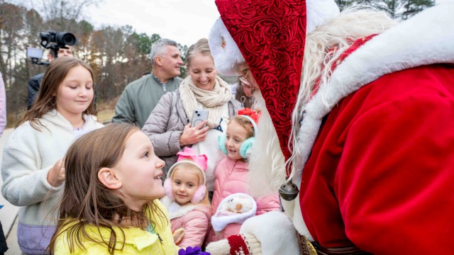 Santa Claus greets children outdoors, sharing a joyful moment during a festive event on a cloudy day.