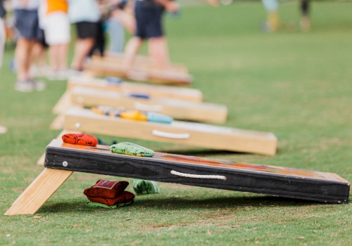 People playing cornhole on a grassy field, boards set up with bean bags ready to toss in the distance.