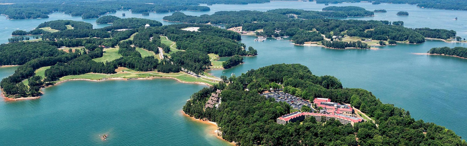 The image shows an aerial view of a lush, forested area surrounded by a large body of water with several small islands and a building complex.