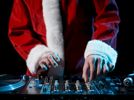 A DJ wearing a red Santa coat is mixing on a turntable and mixer, hands on the controls.