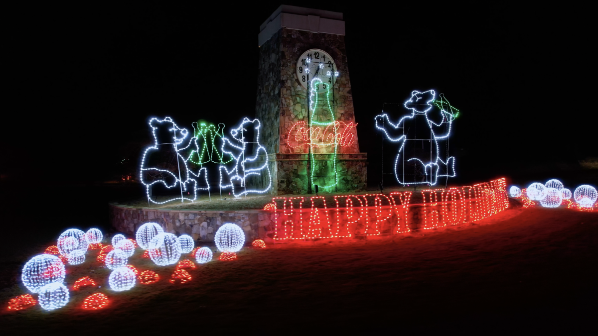 Bright holiday lights: glowing snowmen and figures around a clock tower, with a red “HAPPY HOME” display and glowing snowballs along the ground.