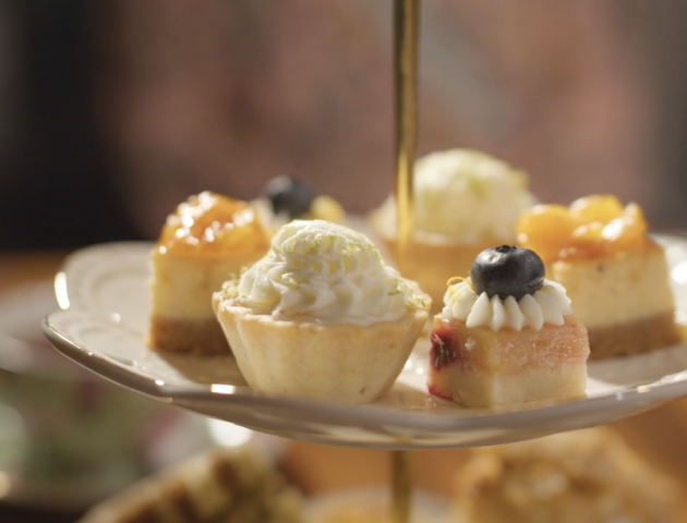 A tiered dessert stand holds bite-sized cakes and cupcakes topped with swirls of cream, berries, and glossy glaze, arranged for a sweet display.