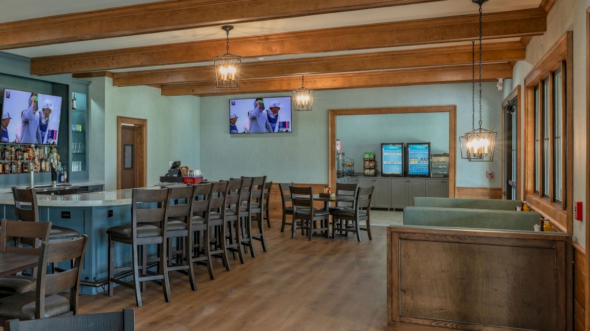 A cozy restaurant interior with wooden beams, multiple TV screens showing a sports event, and a snack/refreshment area.