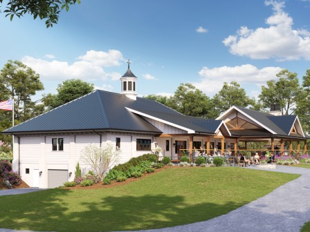 A large modern building with a dark metal roof and cupola sits amid green lawns and trees, with outdoor seating and a person walking nearby.