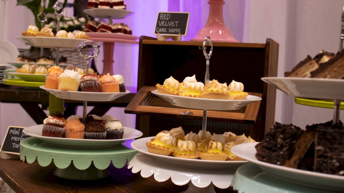 A dessert table with cupcakes, mini tarts, brownies, and assorted pastries on tiered stands and plates, displayed on a wooden table.