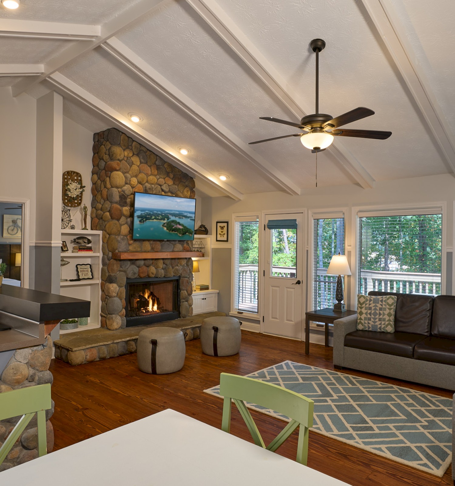 A cozy living room with a stone fireplace, TV, large windows, and modern furniture in a bright, open space.