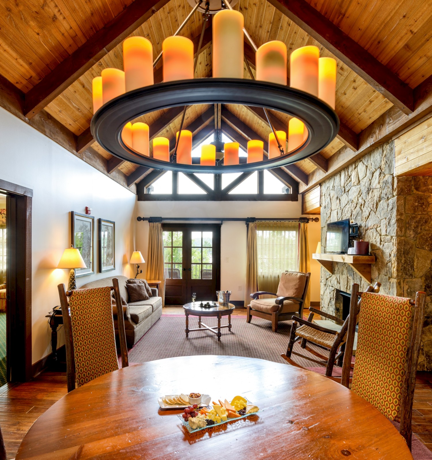 A cozy living and dining room in a rustic cabin with wood accents, a stone fireplace, and warm lighting.