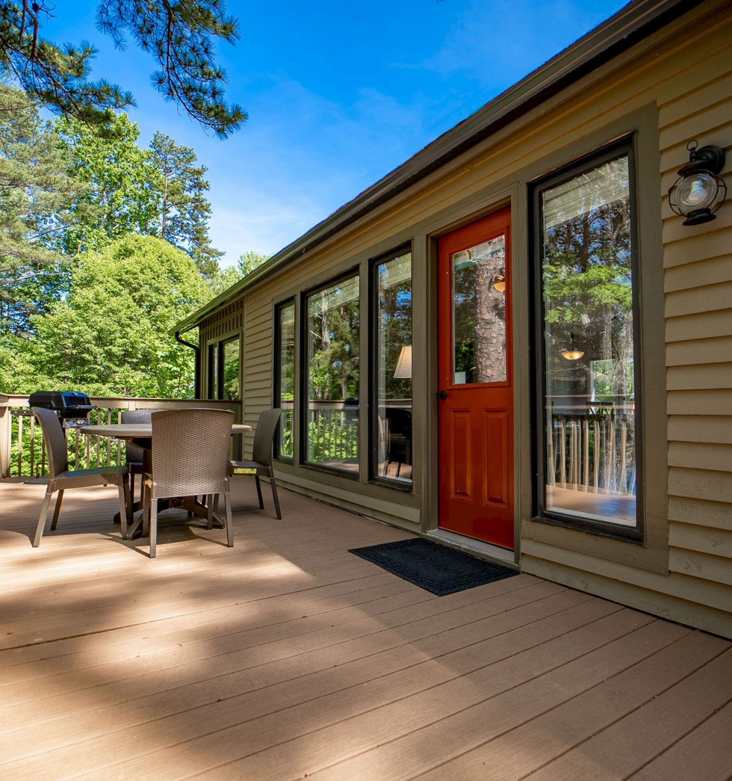 A wooden deck with a table and chairs, overlooking trees, next to a house with red doors.