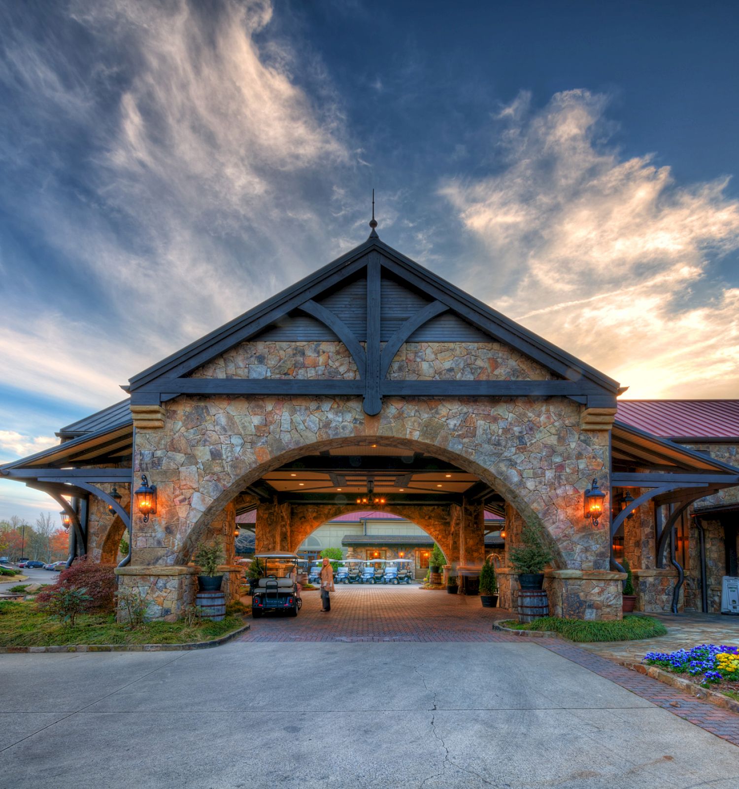 Stone entrance of a building with archways at sunset, sky with dramatic clouds, and illuminated interior.