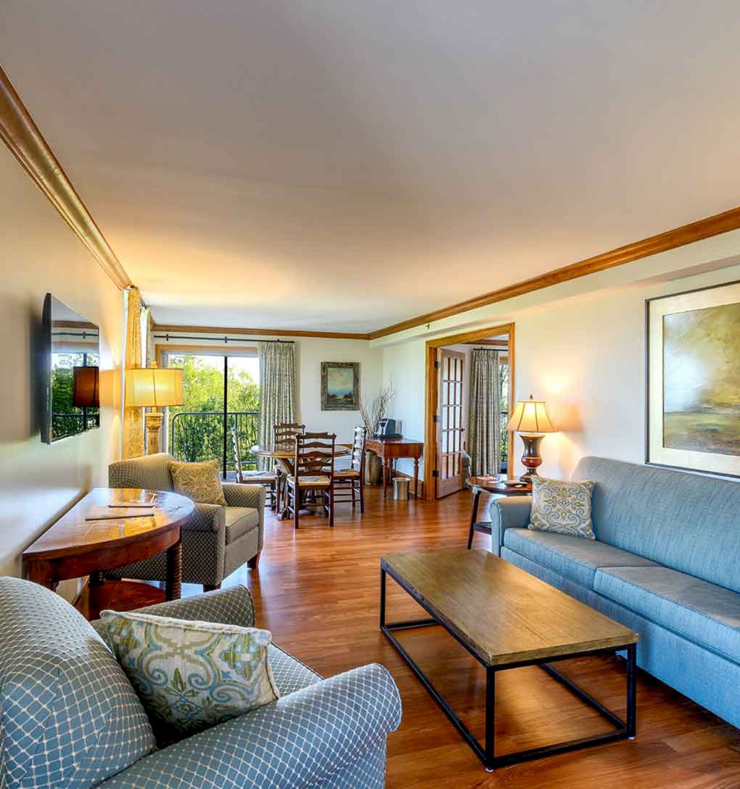 Cozy living room with blue sofa, chairs, artwork, and a view into the adjoining rooms.