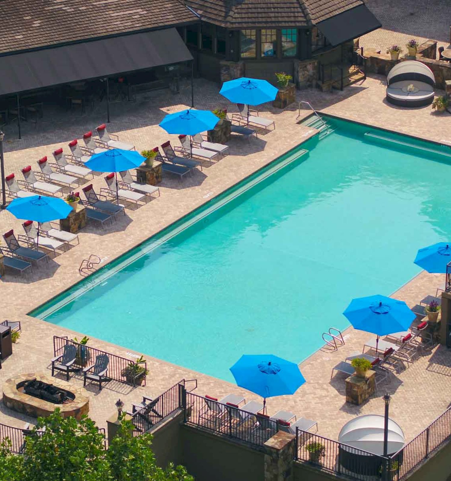 An outdoor pool with blue umbrellas, loungers, and surrounding buildings.