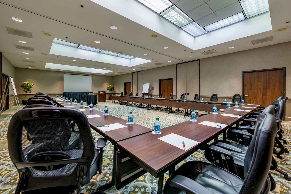 The image shows a conference room with a U-shaped table arrangement, chairs, notepads, pens, and bottled water set up for a meeting or presentation.
