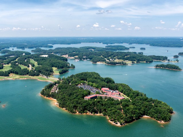 Aerial view of lush green islands surrounded by blue waters, with buildings visible on one island and a few boats in the water.