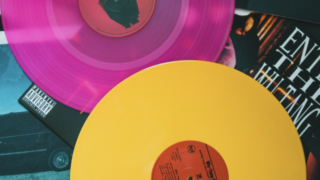 Two colored vinyl records, one pink and one yellow, lie atop album covers, featuring various designs and text.
