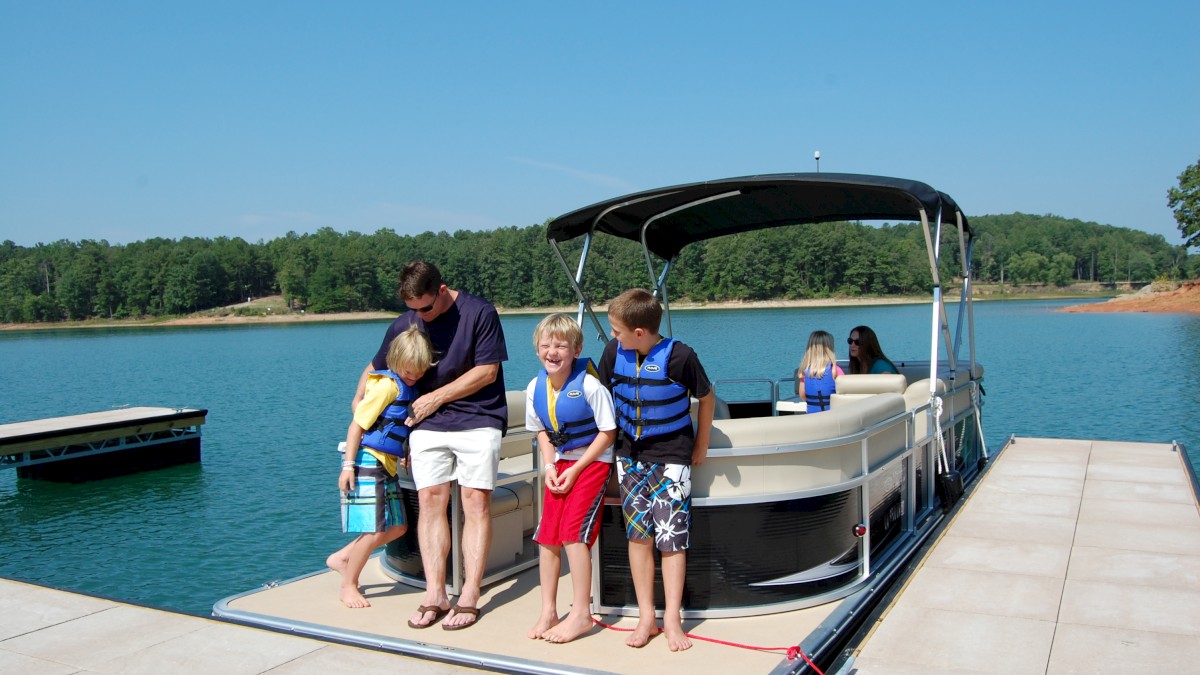 A family is enjoying a day at the lake, with kids in life jackets on a boat docked near the shore on a sunny day.