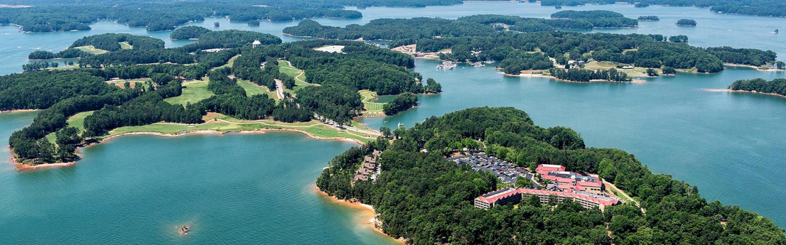 The image shows an aerial view of a large body of water with numerous forested islands, and buildings on one island surrounded by lush greenery.