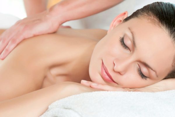 A person is lying down with eyes closed, receiving a relaxing back massage, with a serene expression on the face and a clean, comfortable setting.