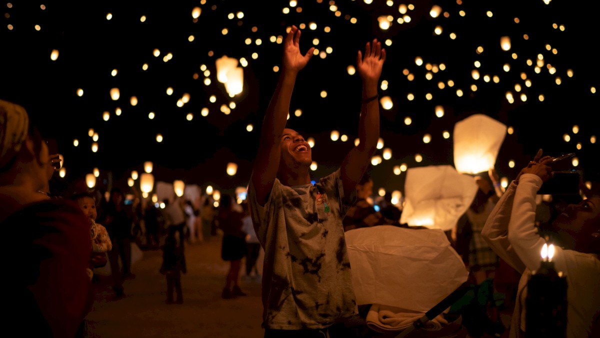 People releasing sky lanterns during a nighttime event, celebrating or commemorating something with a joyful atmosphere.