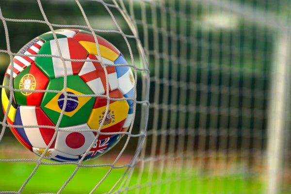 A soccer ball with flags of various countries is stuck in the net at the goal.