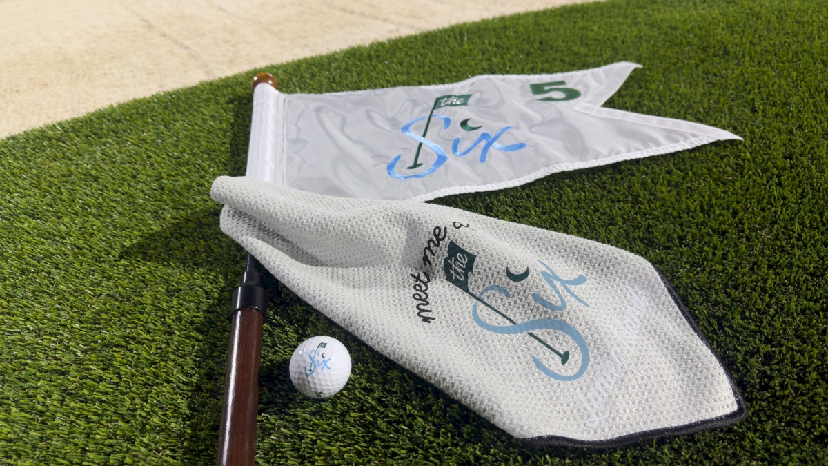 Golf flags, a ball, and a golf club on a green with the slogan 