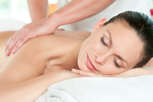 A person is relaxing and receiving a back massage, lying on a towel with eyes closed, creating a peaceful atmosphere.