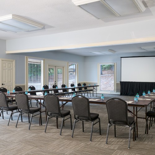 A conference room with a U-shaped table setup, many chairs, a projection screen, and water bottles on the table, ready for a meeting.