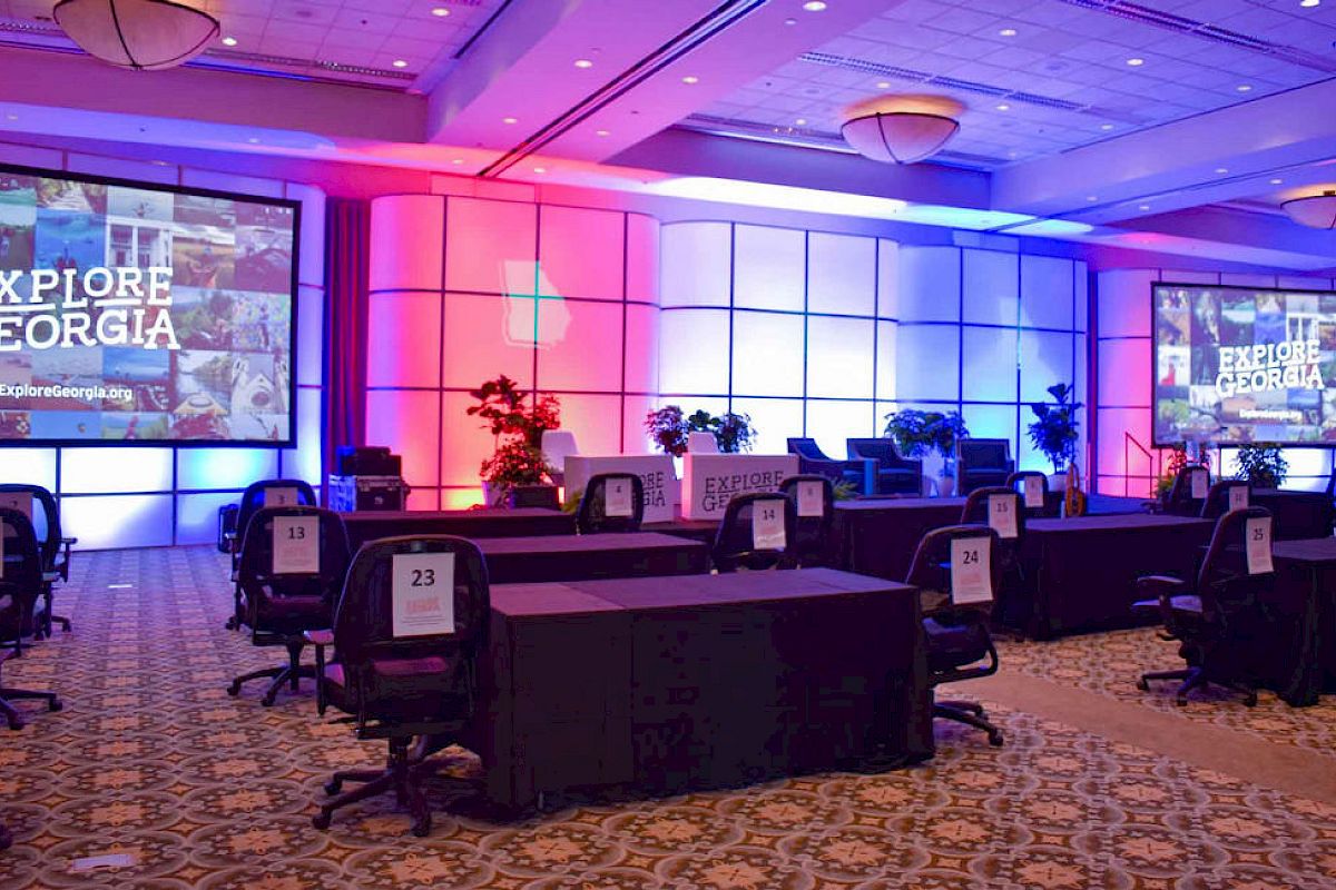 The image shows a conference hall set up with tables, chairs, screens displaying 
