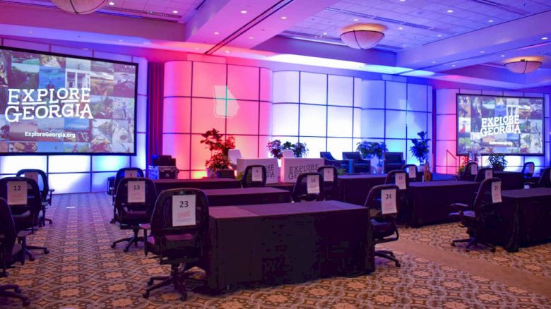 The image shows a conference hall set up with tables, chairs, screens displaying 