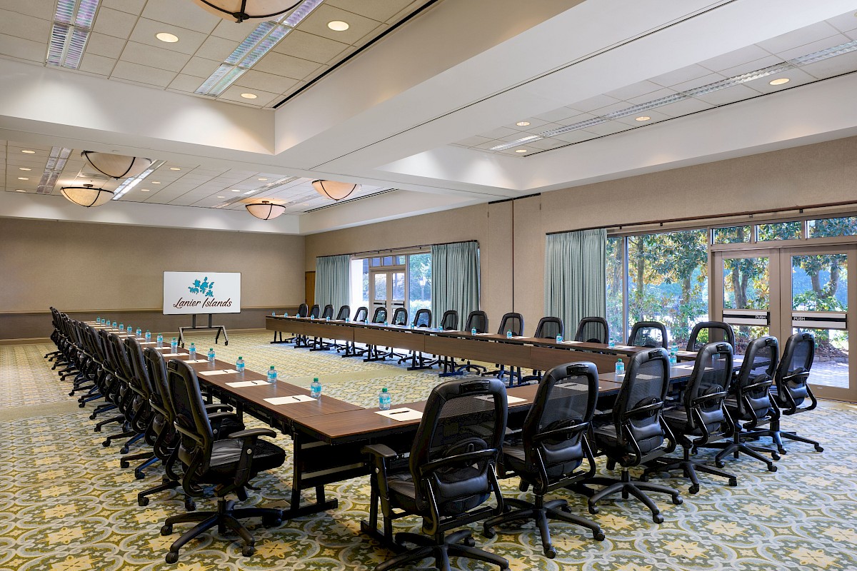 A large, well-lit conference room with a U-shaped table, many black office chairs, water bottles, and a screen at the front, ready for a meeting.