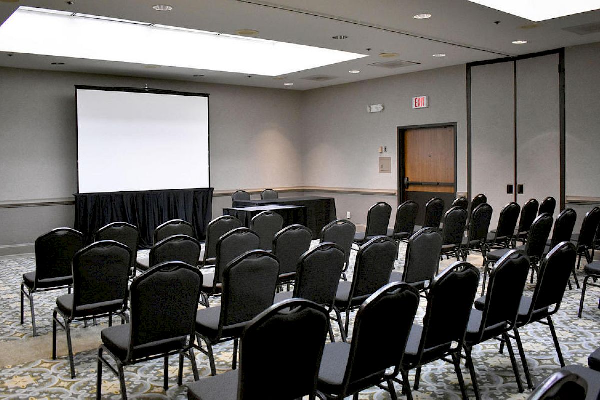 This image shows a conference room with rows of empty chairs facing a screen and projector, ready for a presentation or meeting.