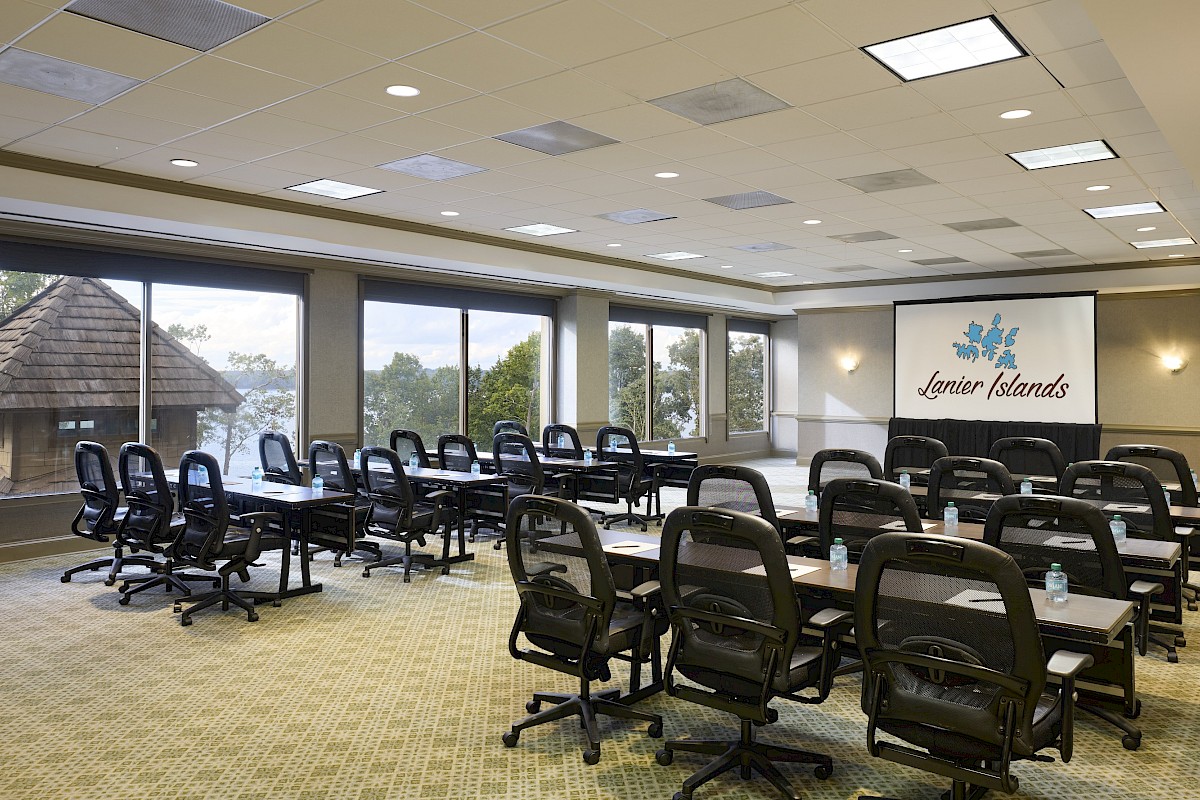 A bright conference room with rows of swivel chairs around long tables, large windows, and a sign reading “Lazier Islands” on the wall.