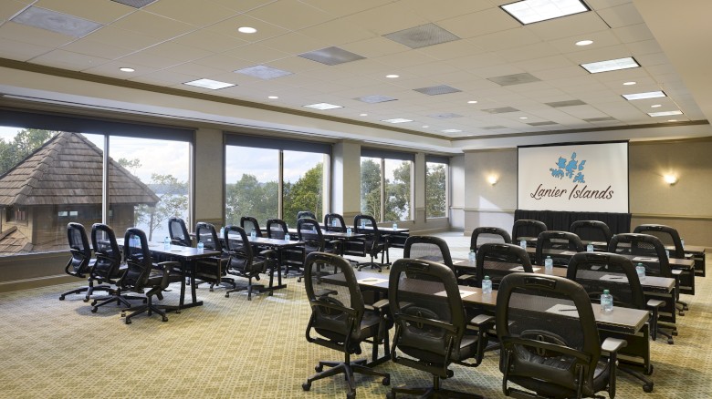 A bright conference room with rows of swivel chairs around long tables, large windows, and a sign reading “Lazier Islands” on the wall.