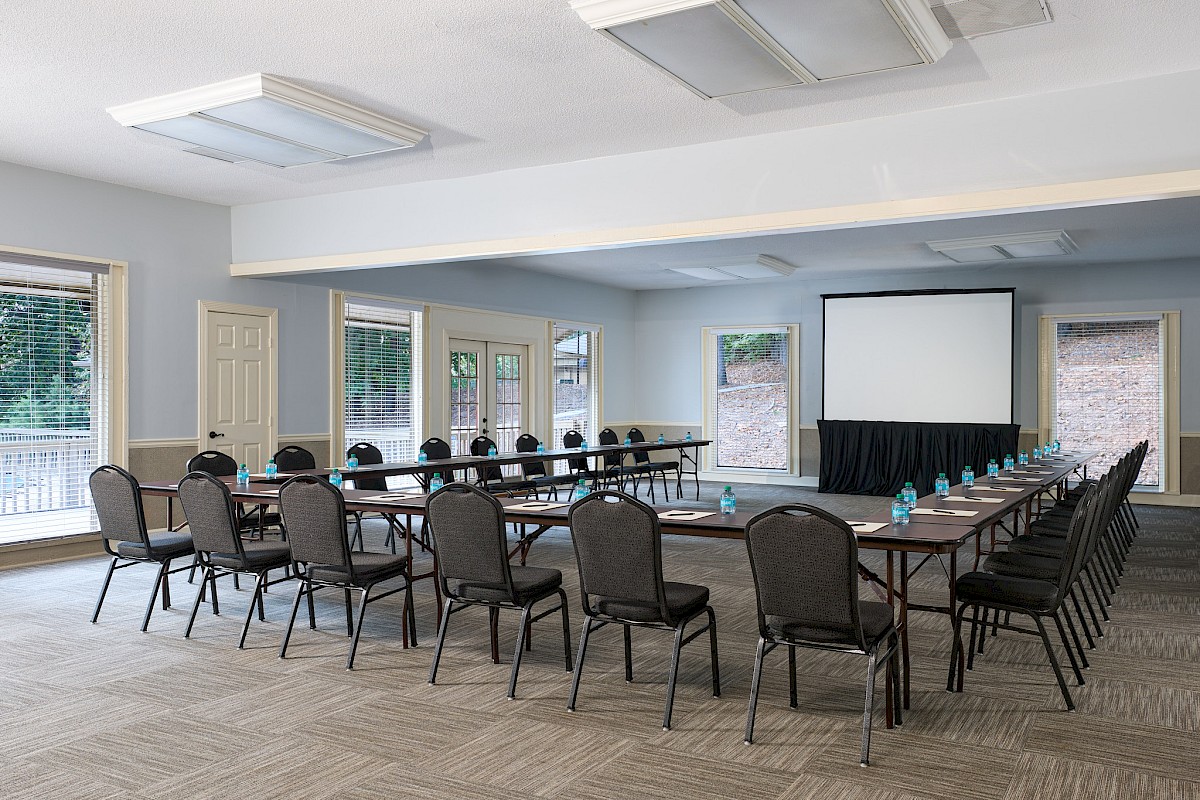 A conference room with a U-shaped table setup, many chairs, a projector screen, and water bottles on the table, ready for a meeting.